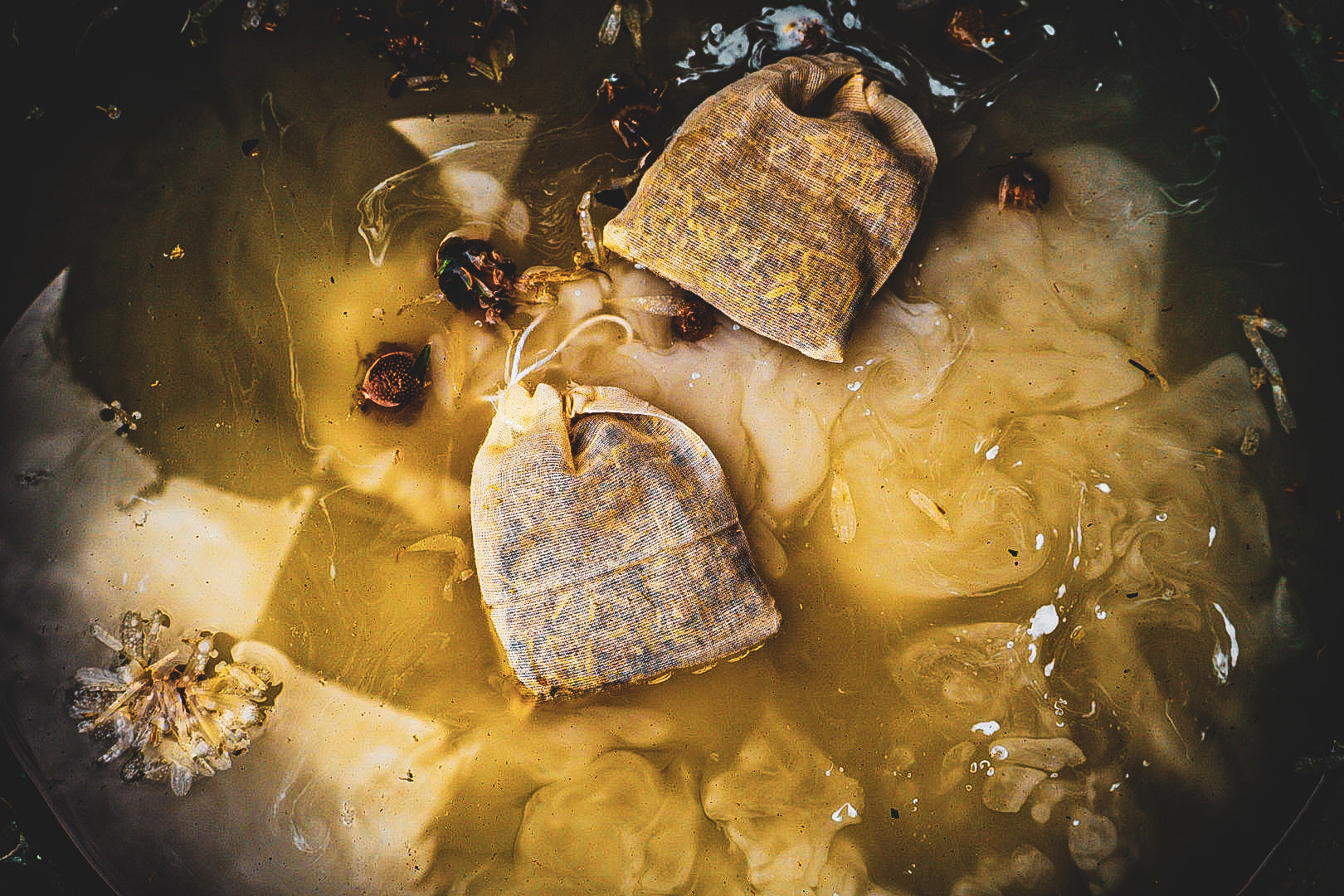 First Fire herbal bath bags steeping in golden water with botanicals