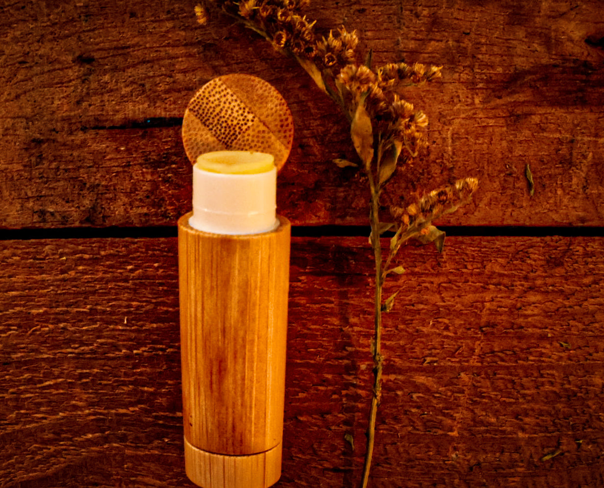 The Gentle Guardian Pocket Salve Stick — bamboo tube on warm wood with dried goldenrod